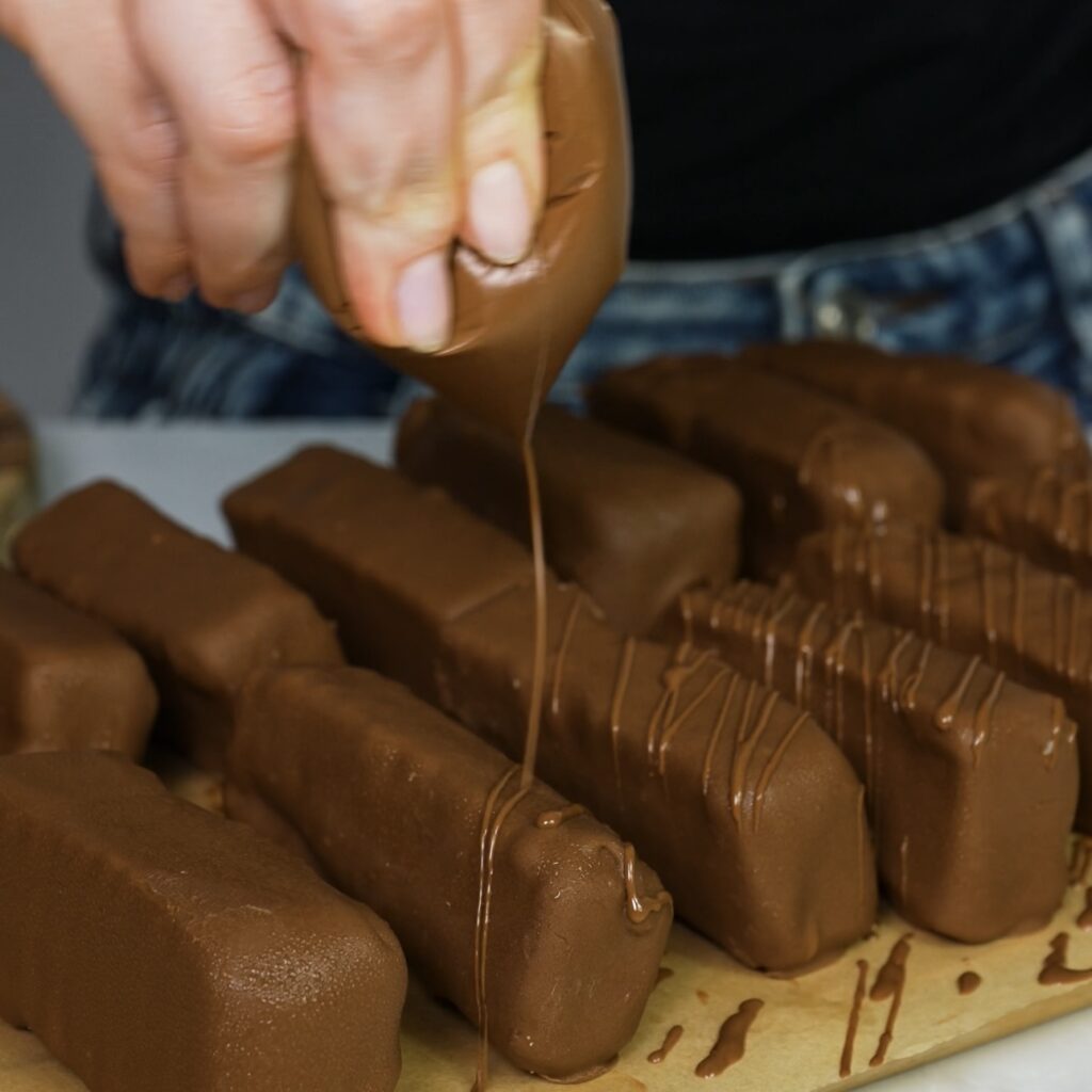 Drizzling melted chocolate over the bars on parchment paper