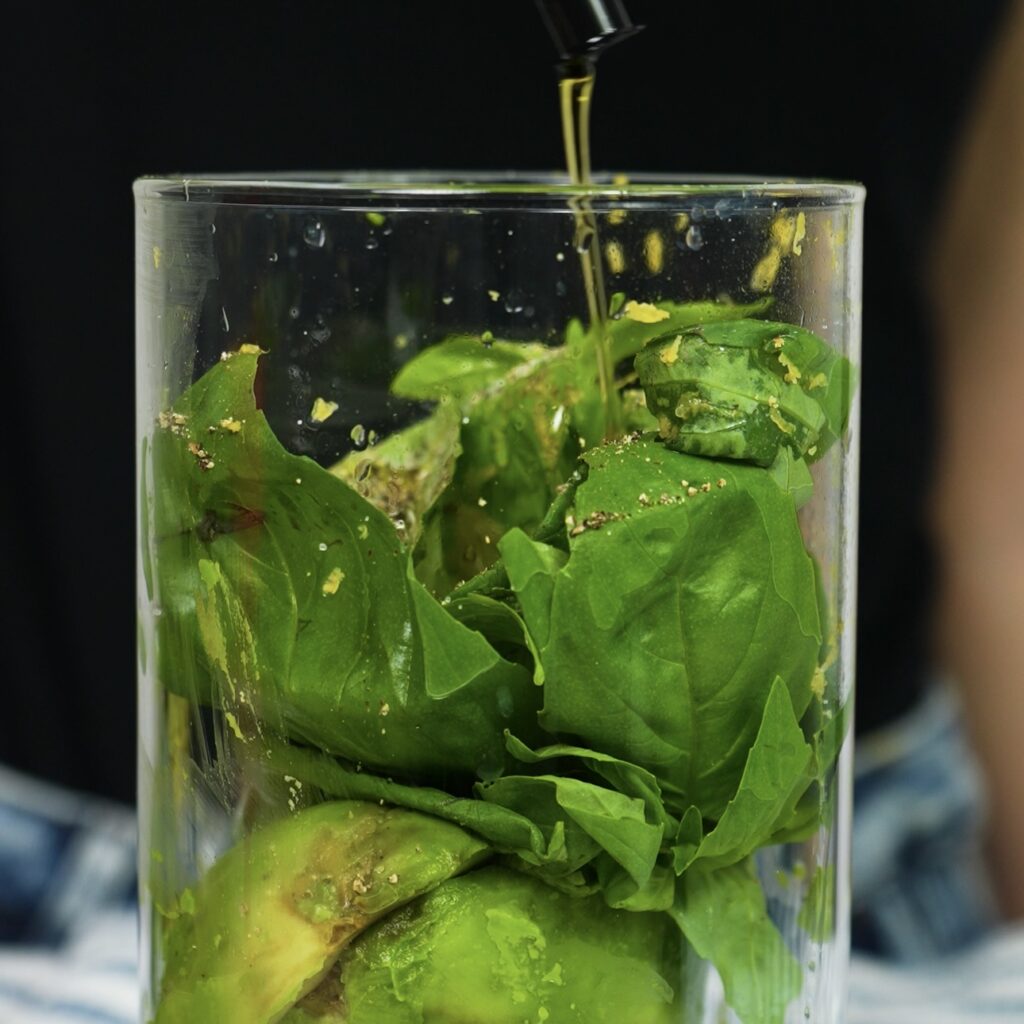 Fresh avocado, basil, garlic, lemon zest, lemon juice, olive oil, salt, and pepper ready to be blended in a food processor