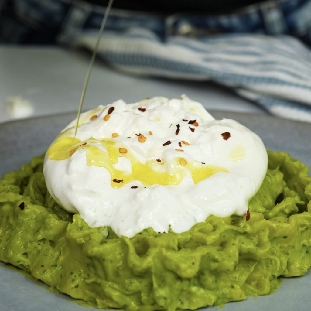 Drizzling golden olive oil over creamy burrata cheese on a serving plate