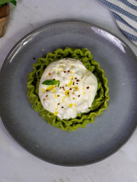 Avocado and burrata pasta served on a white plate, garnished with basil leaves and chilli flakes