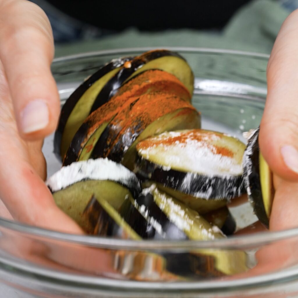 Mixing aubergine slices with seasoning in a bowl