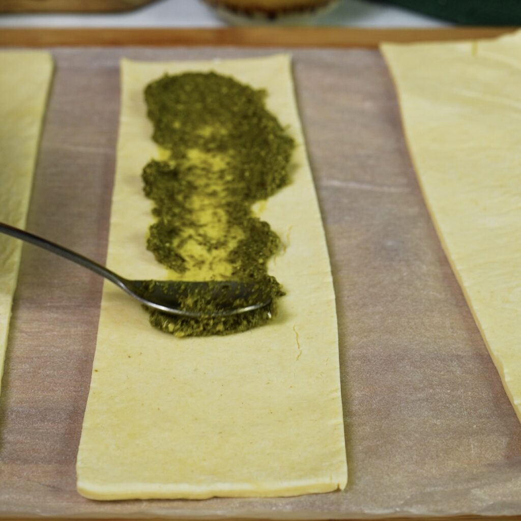 Spreading basil pesto on puff pastry strips.