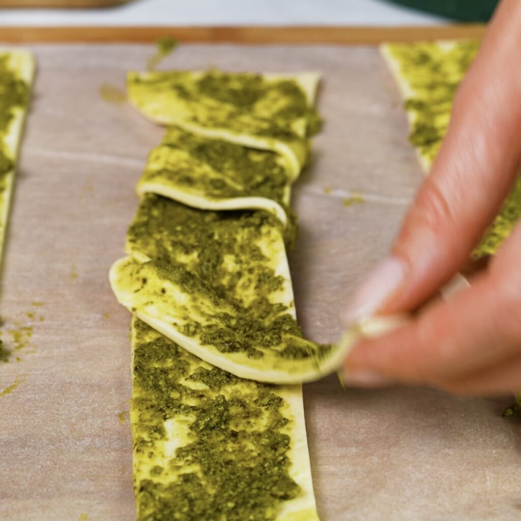 Twisting puff pastry strip filled with pesto.