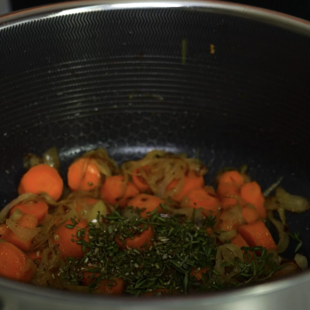 Onions, carrots, and herbs caramelising in a pot.