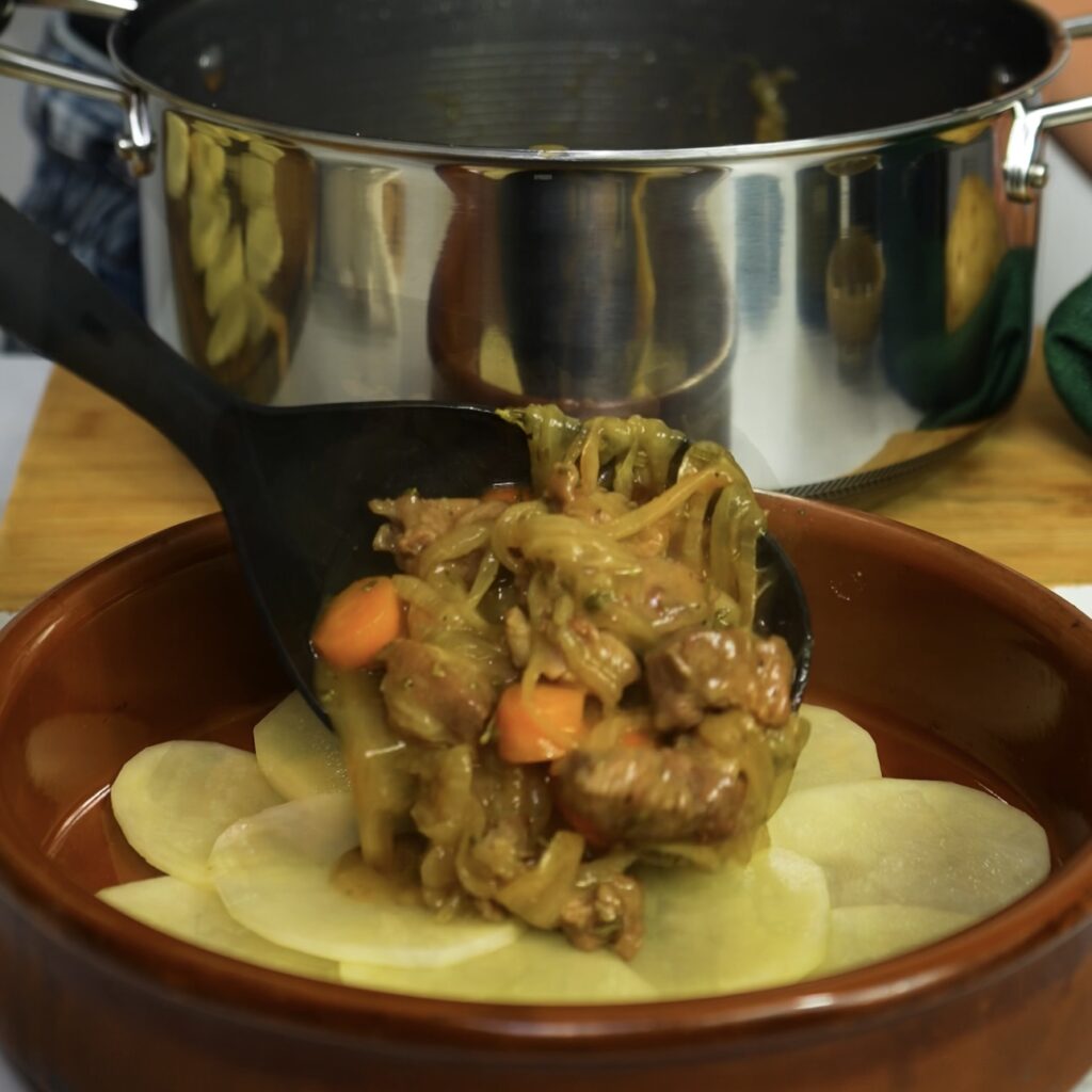 Adding lamb sauce over a layer of potatoes in a baking dish