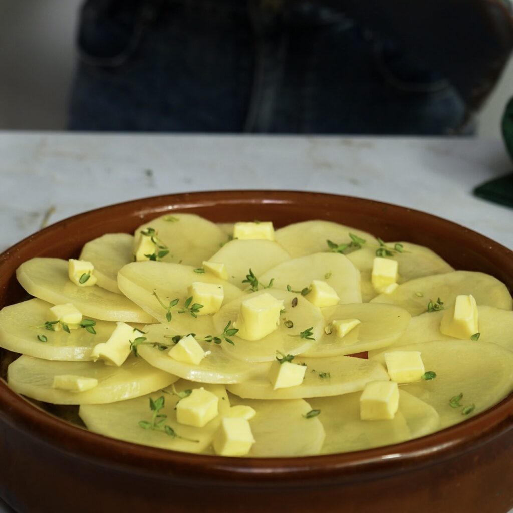 Lancashire Hotpot topped with butter, and thyme, ready for baking.