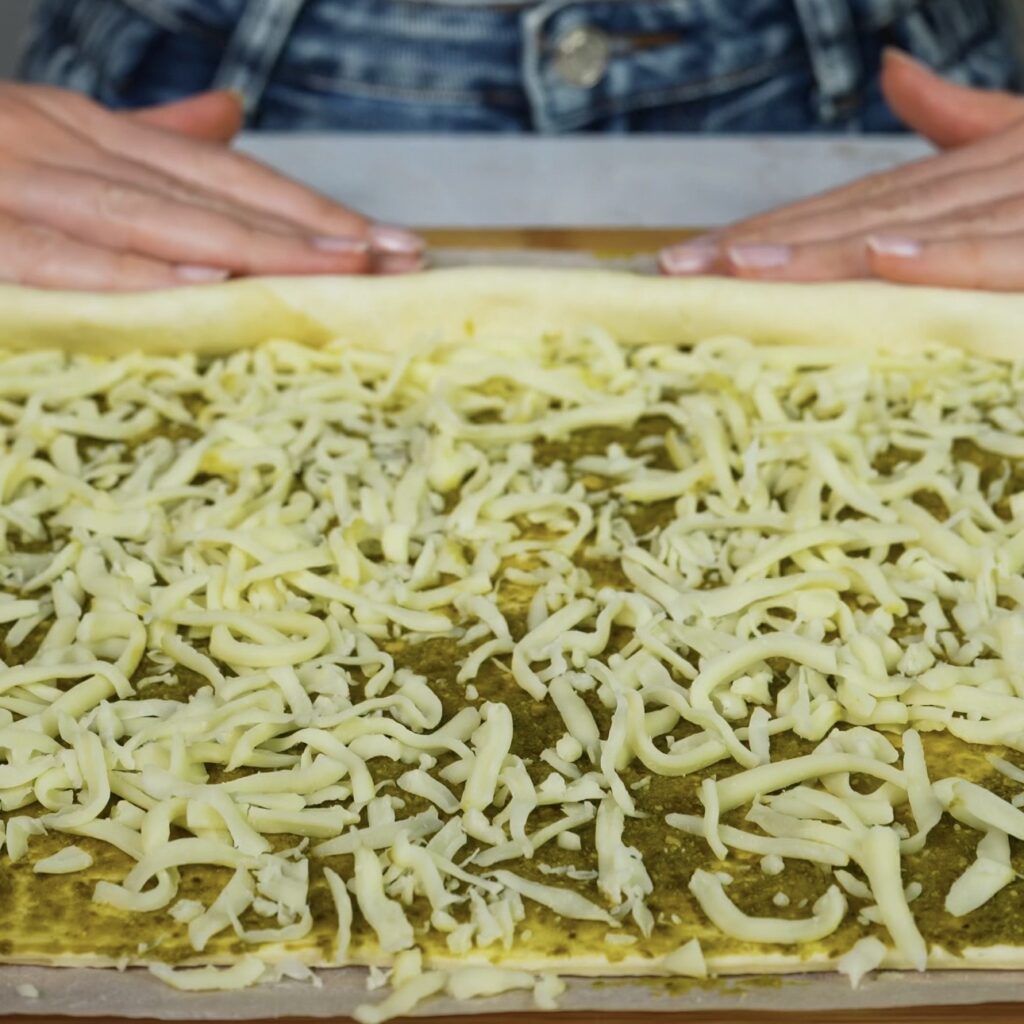 Mozzarella sprinkled evenly over puff pastry spread with pesto.