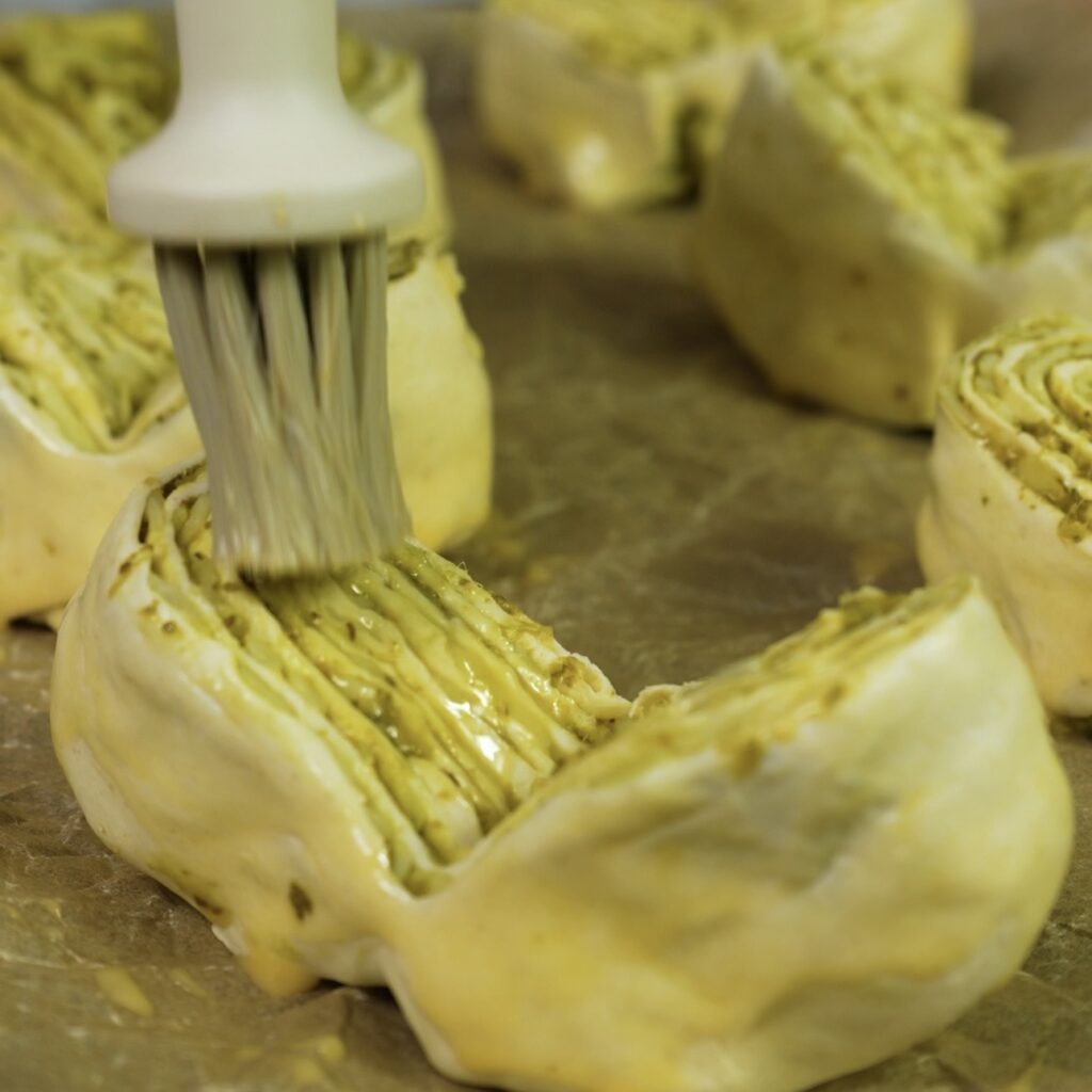Brushing the shaped puff pastry buns with egg wash before baking.