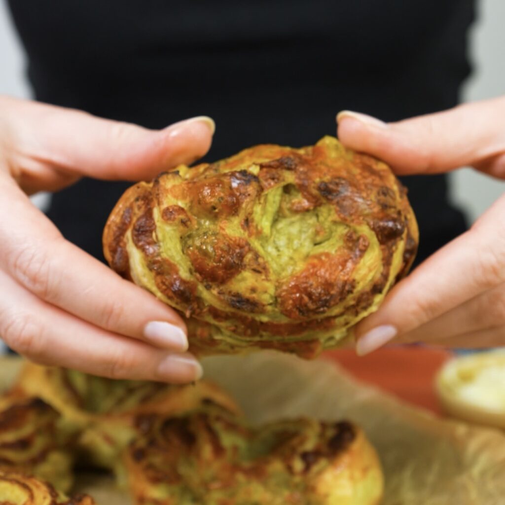 Hands holding a freshly baked Cheesy Pesto Puff Bun