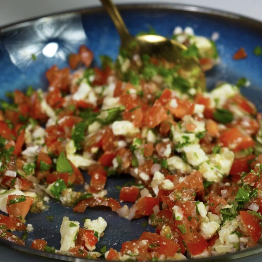 Mixing chopped cherry tomatoes, feta, shallot, and coriander in a bowl with a spoon
