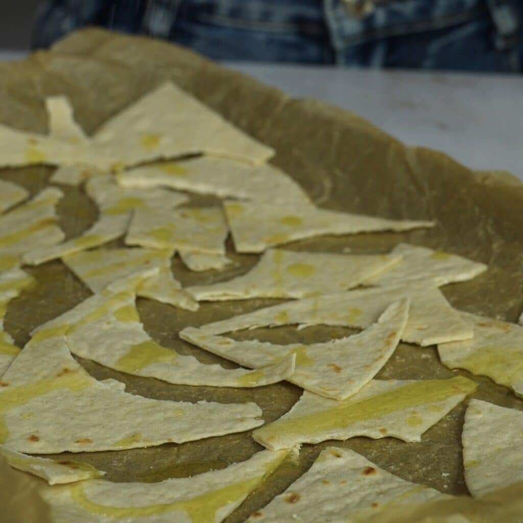 Tortilla pieces on a baking tray drizzled with olive oil and sprinkled with salt before baking