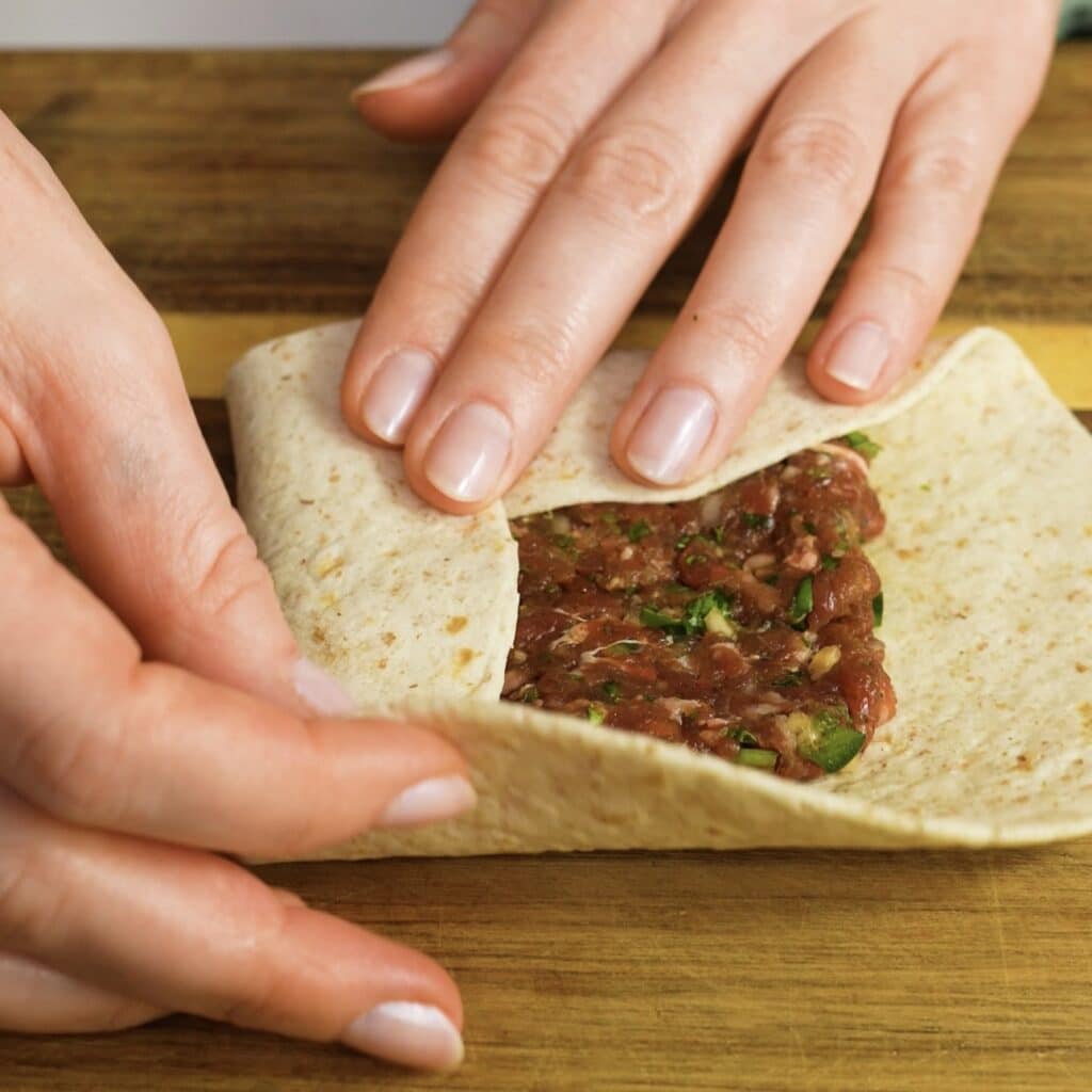 Folding the tortilla edges over the beef filling to form a parcel.
