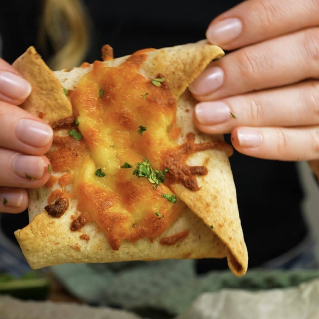 Hands holding a baked tortilla parcel with melted mozzarella.