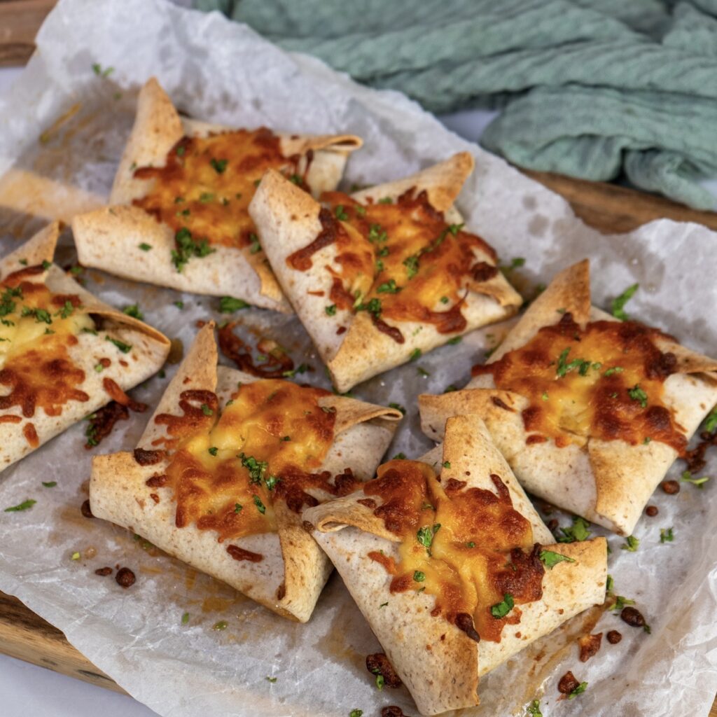 Baked tortilla parcels served on a wooden board.