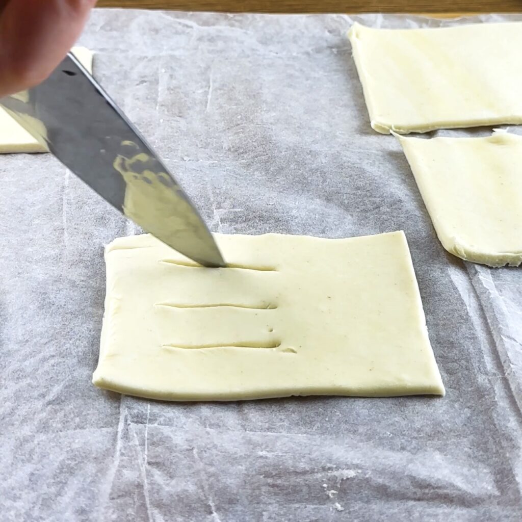 Cutting three parallel lines into puff pastry for mini sausage puffs
