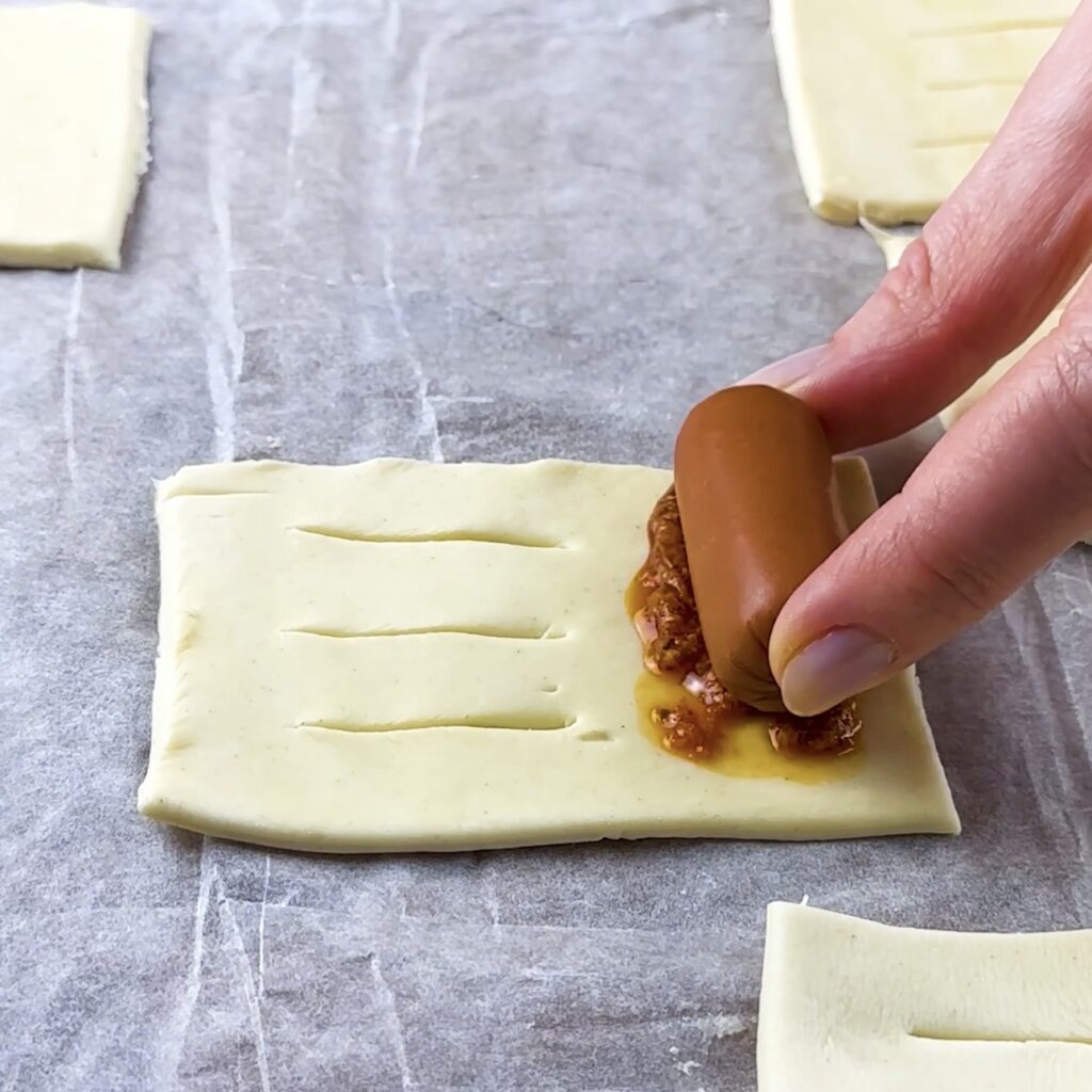 Placing a cocktail sausage on sun-dried tomato pesto on puff pastry
