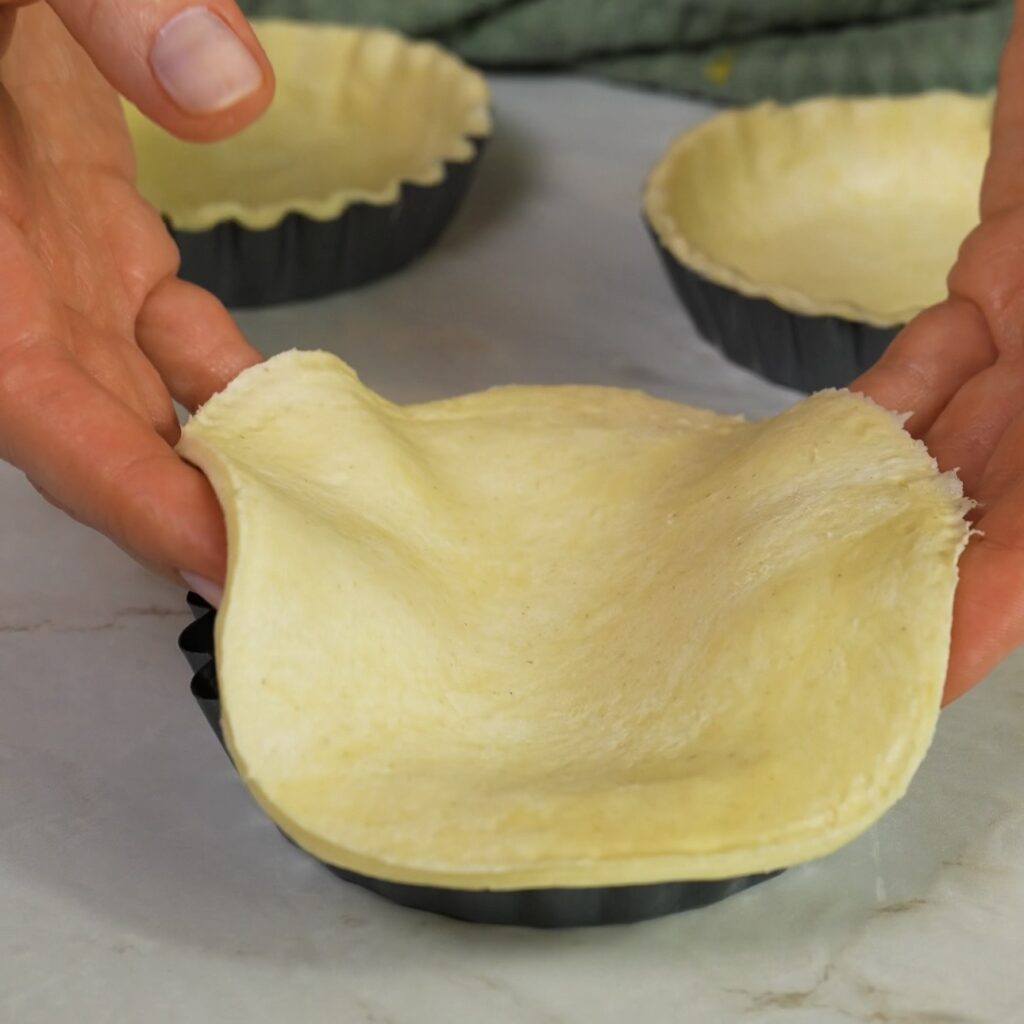 Fitting puff pastry into tartlet tins before adding the frangipane filling