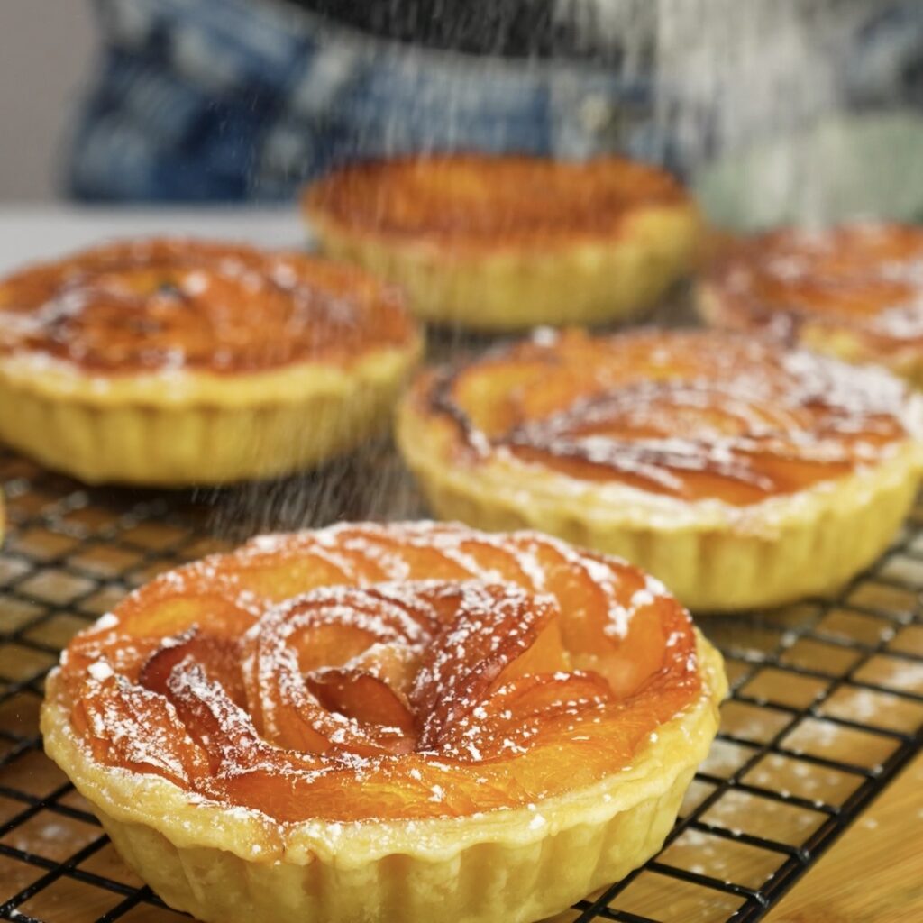 Dusting nectarine frangipane tartlets with icing sugar