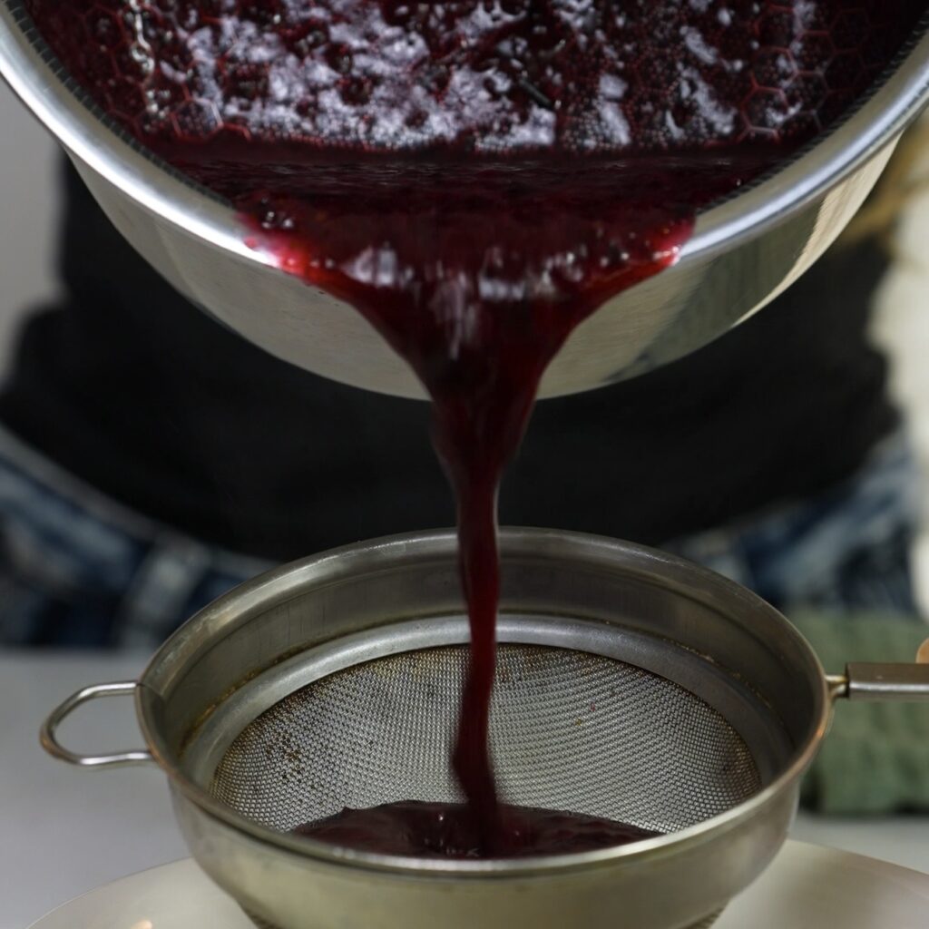 Straining blueberry syrup through a fine sieve to remove skins and seeds