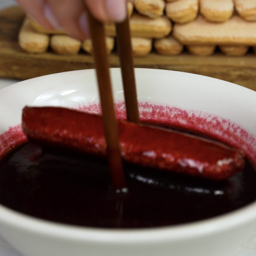 Dipping sponge fingers into blueberry syrup before layering