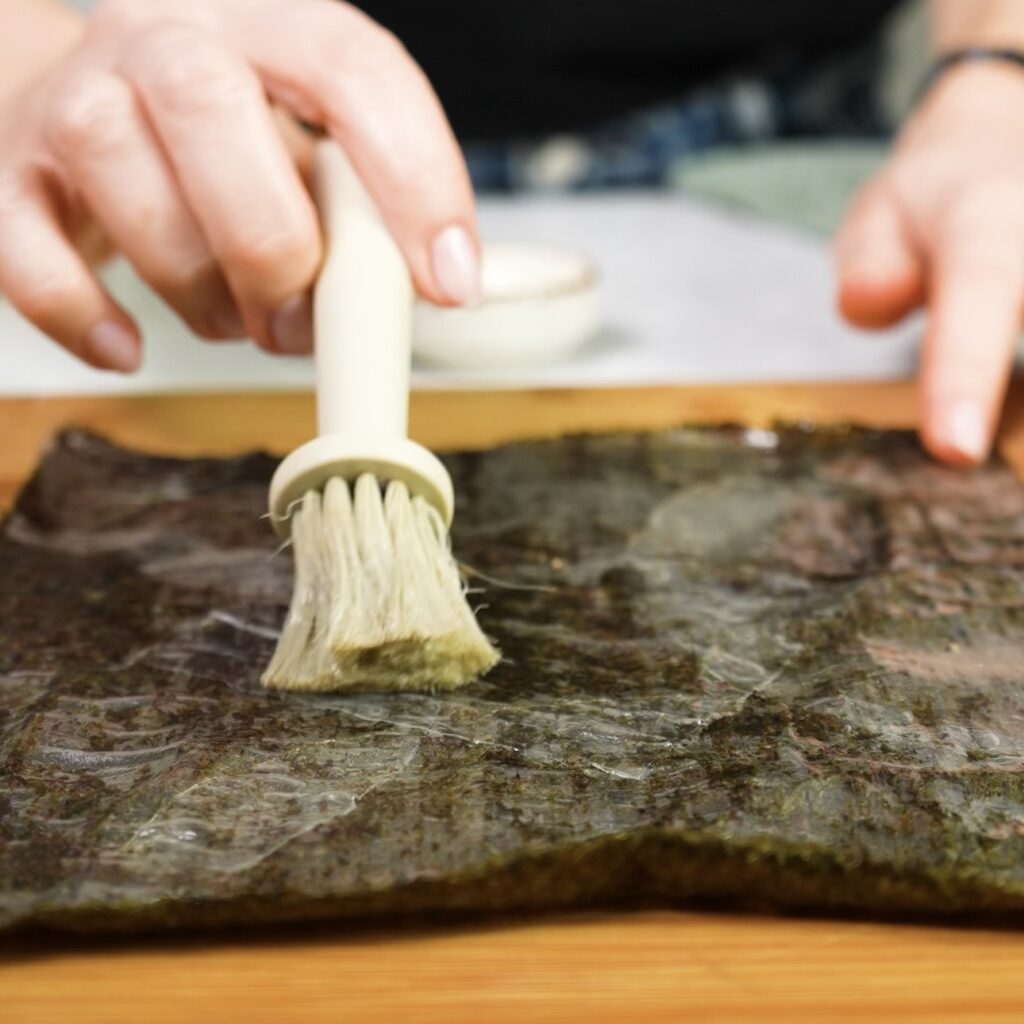 Brushing rice paper with olive oil before flipping the nori base for crispy salmon squares