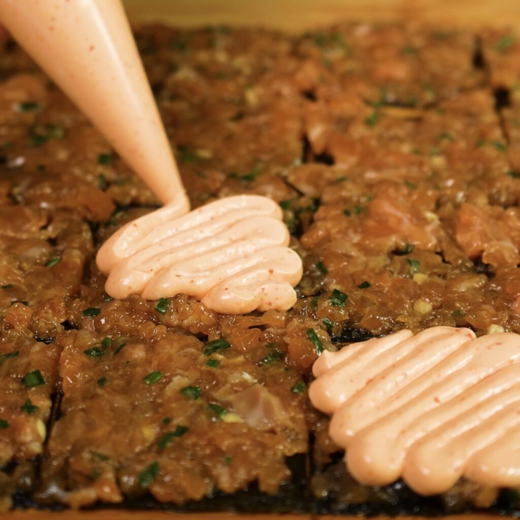 Piping creamy sriracha sauce onto salmon squares before air frying