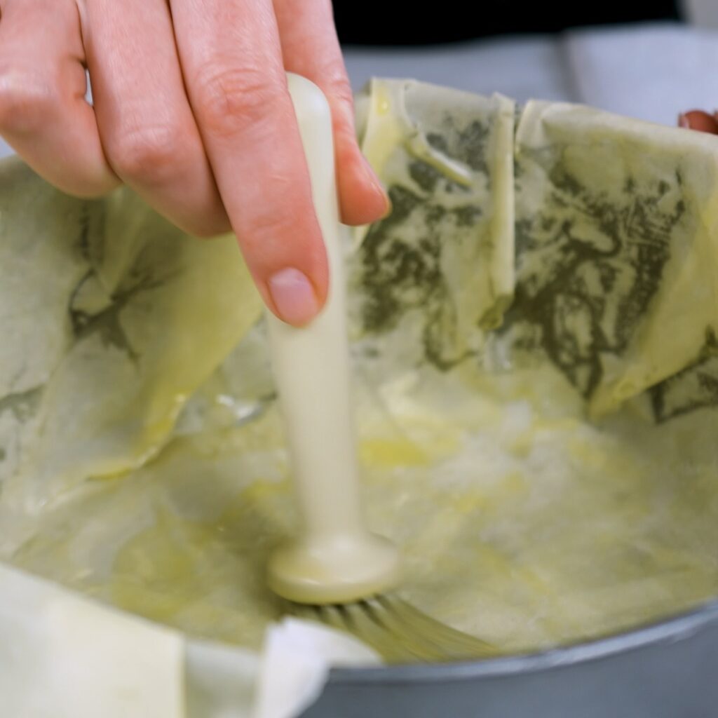 Brushing each layer of filo with butter in a baking tin