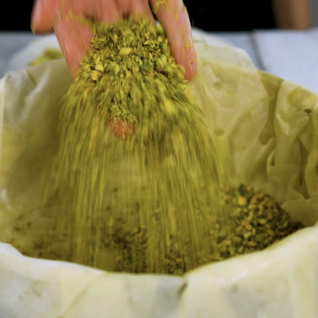 Adding crushed pistachios between buttered filo layers in a baking tin