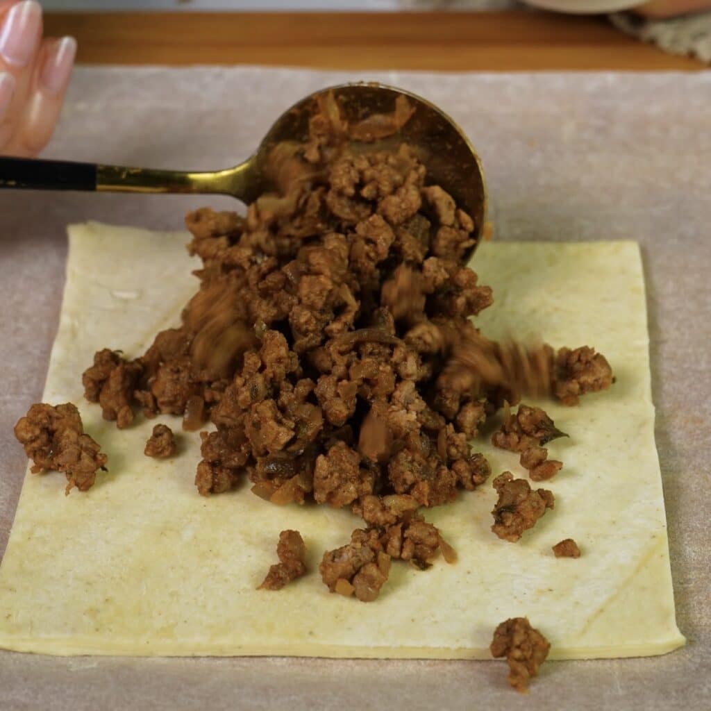 Adding beef filling to puff pastry squares