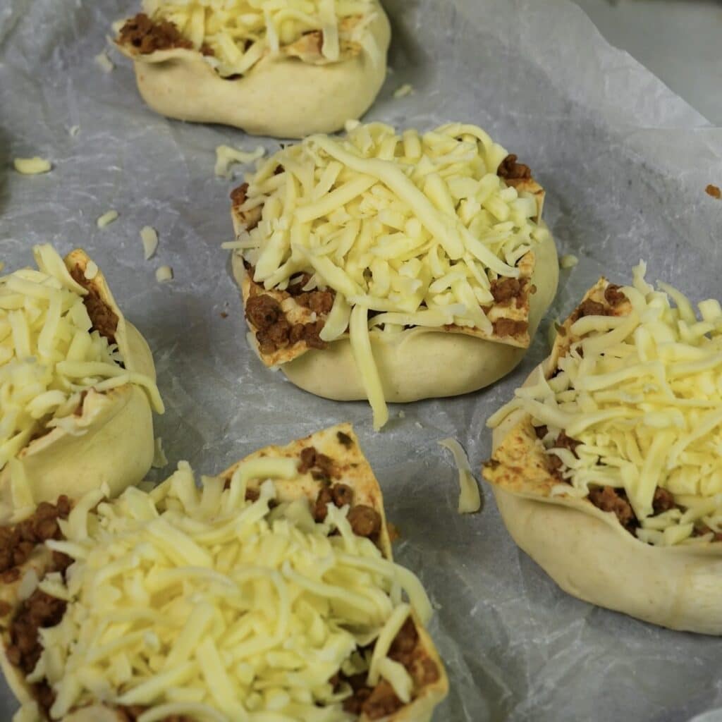 Sprinkling grated mozzarella over puff pastry parcels