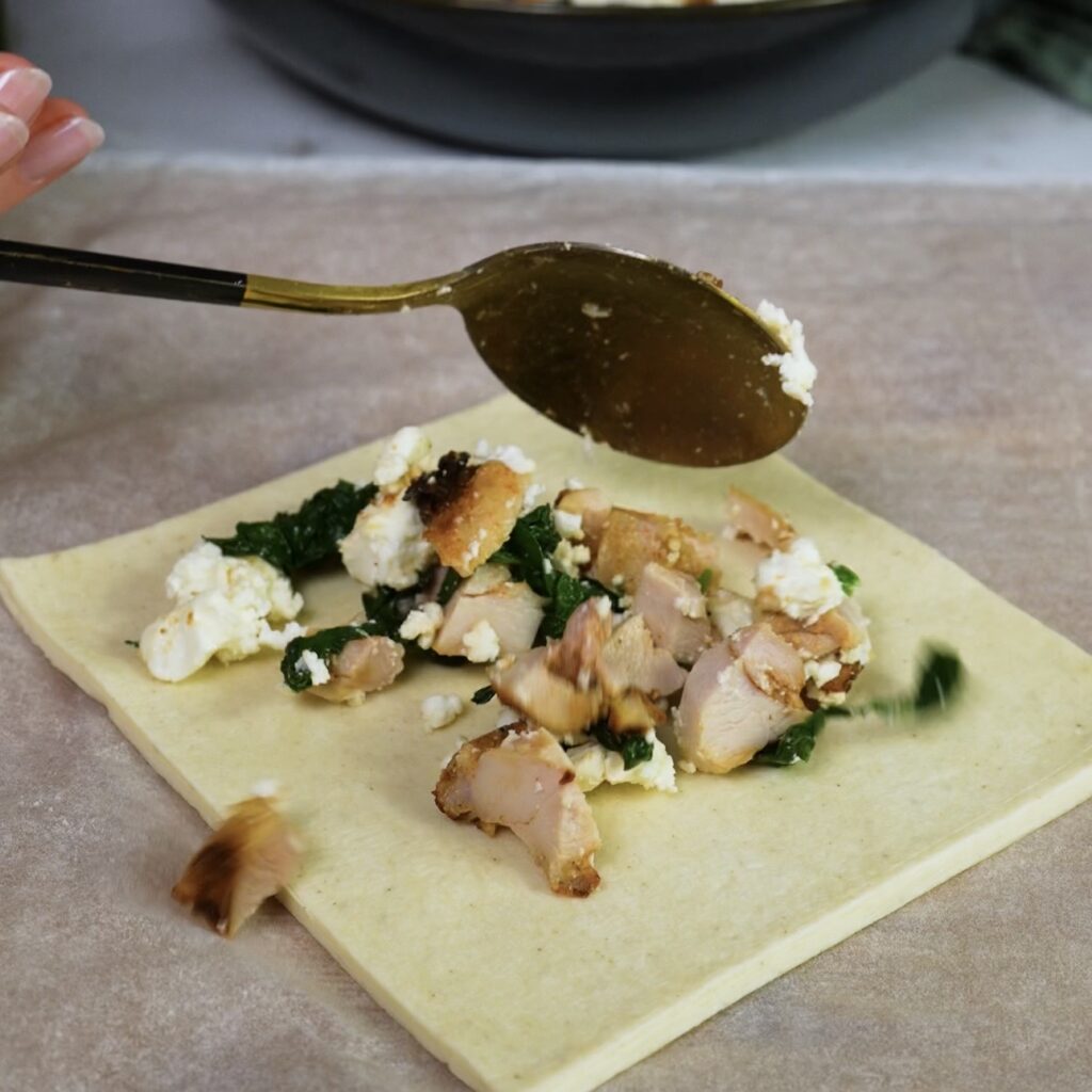 Adding chicken and feta filling to a puff pastry square.
