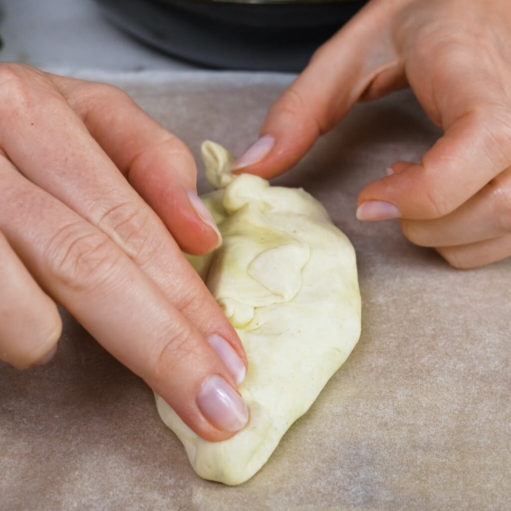 Flattening the pastry parcel and folding the ends inward to shape it.
