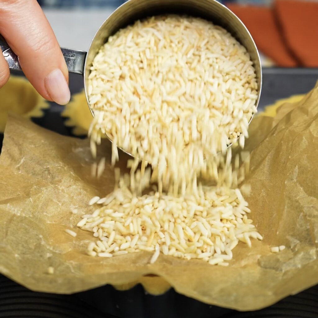Adding uncooked rice to a lined tart shell for blind baking.