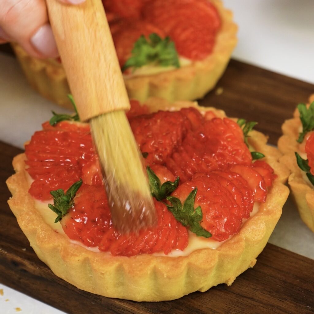 Brushing strawberries with jam glaze on tartlets.