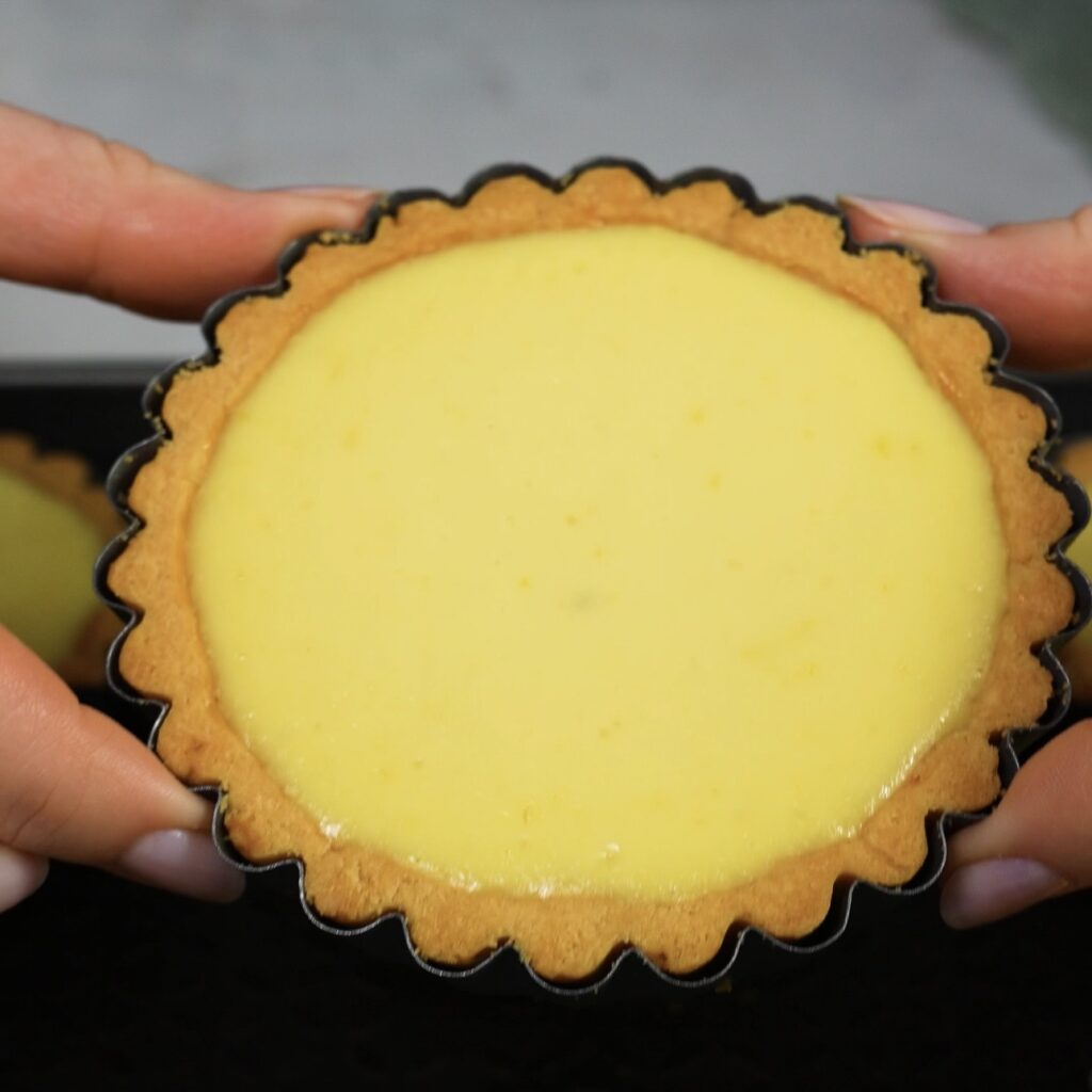 Hands holding a baked ricotta tartlet in a golden pastry shell