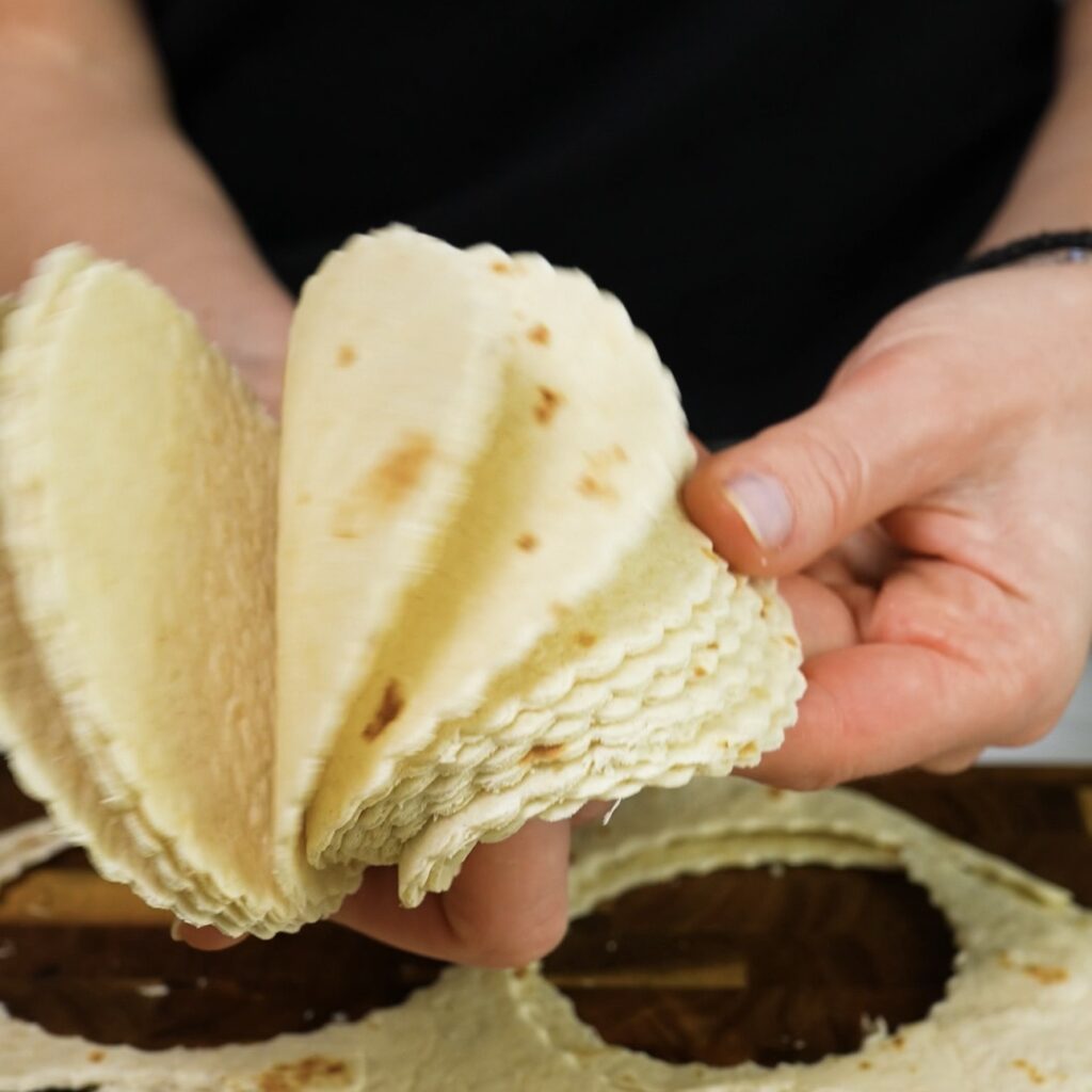 Hands holding tortilla circles cut from flour tortillas