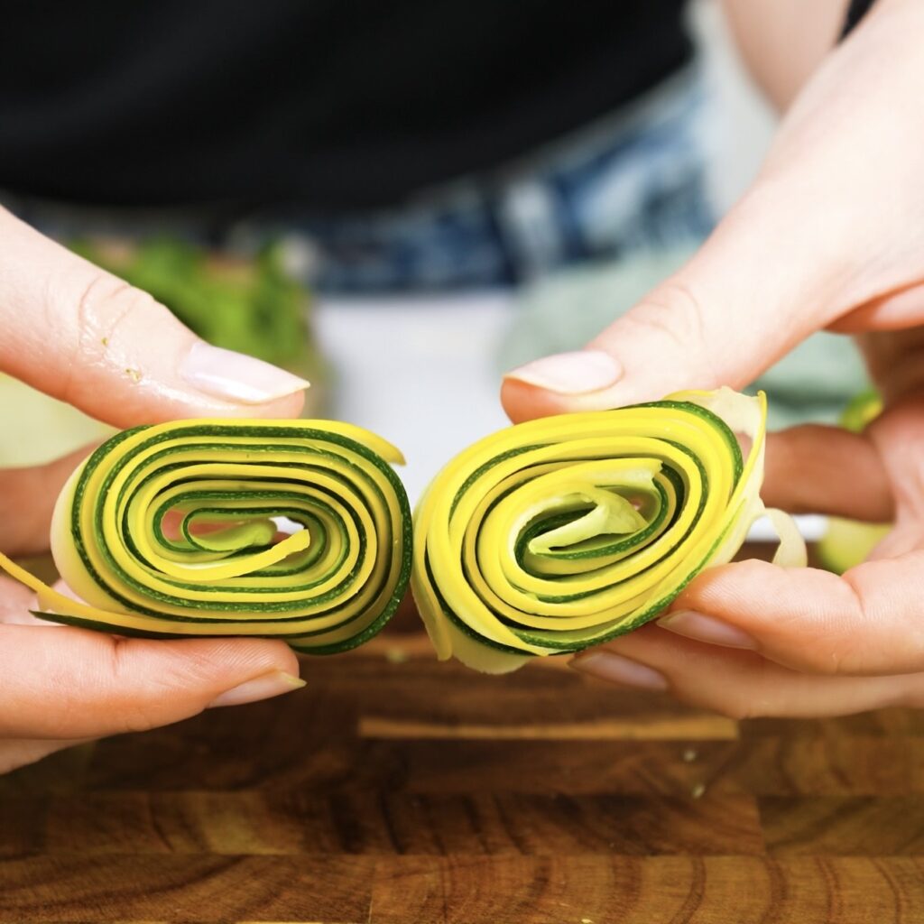 Hands holding courgette and squash spirals cut in half