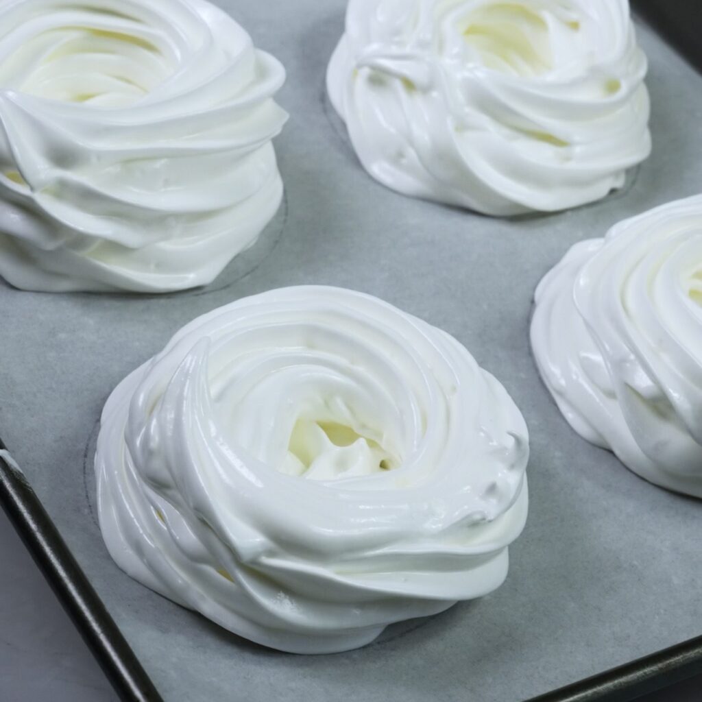 Mini pavlova nests piped onto a parchment-lined baking tray before baking