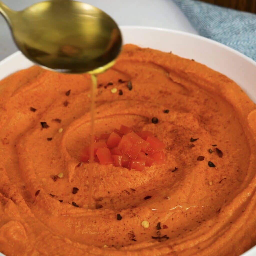 Drizzling olive oil over roasted pepper hummus before serving