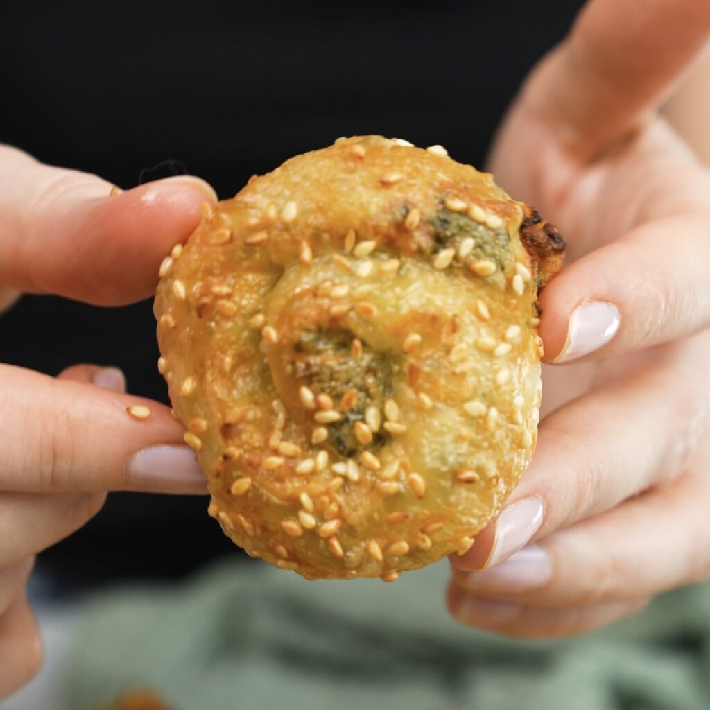Hands holding a freshly air-fried feta and spinach rice paper roll