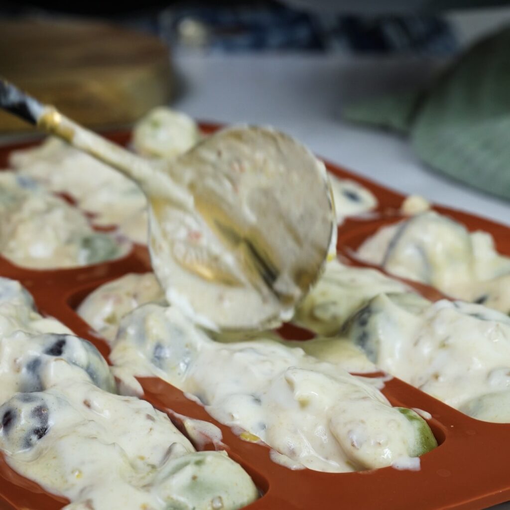 Spoon yogurt and grapes mixture into silicone mould for frozen bars