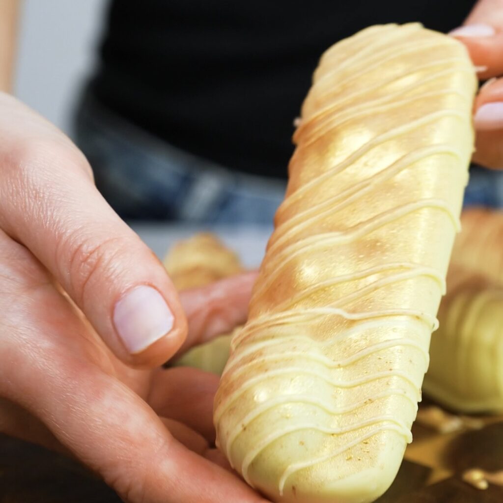 Hands hold a grape yogurt bar coated in chocolate and dusted with gold