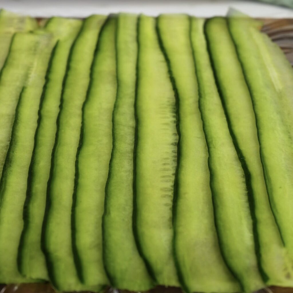 Cucumber strips overlapping on cling film to form a sheet