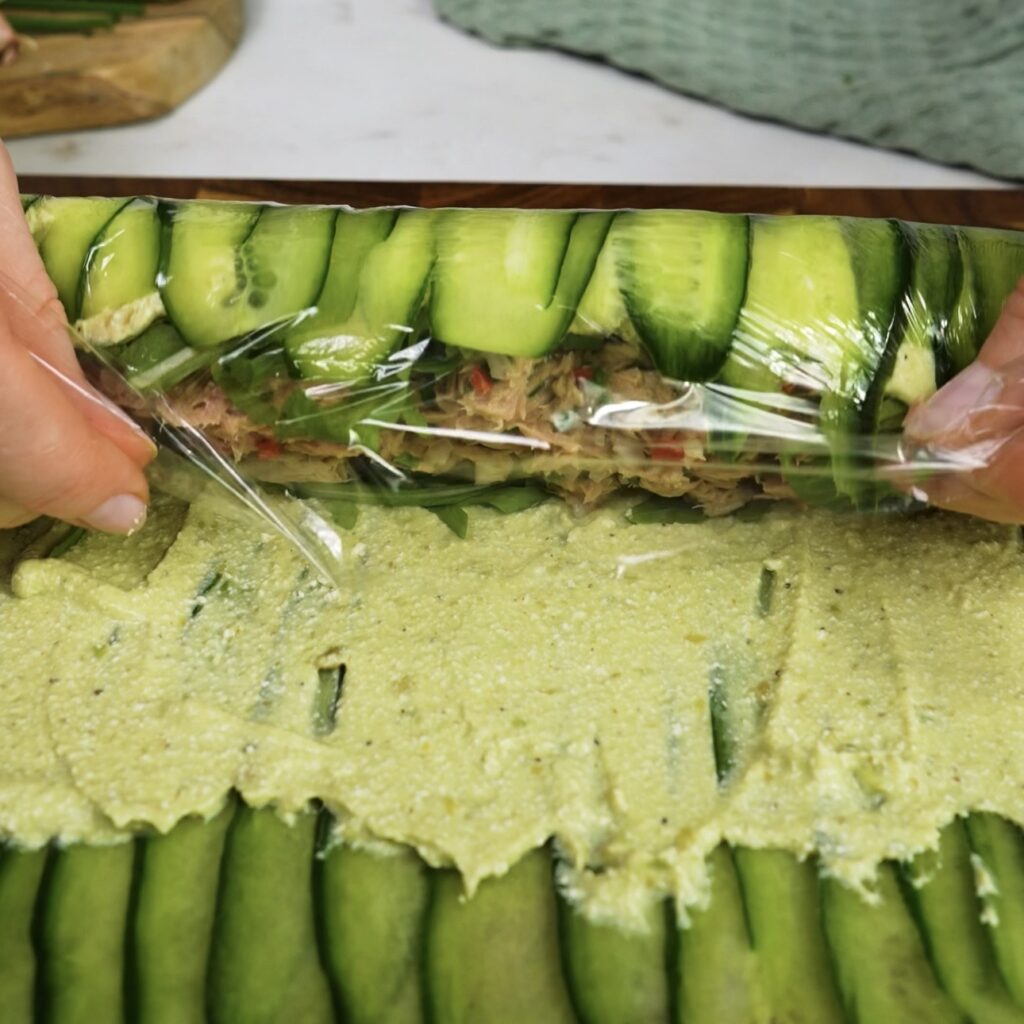 Rolling the cucumber sheet into a tight roll using cling film