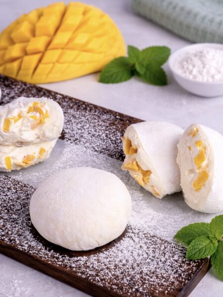 Mango mochi on a wooden board with one piece sliced to show filling