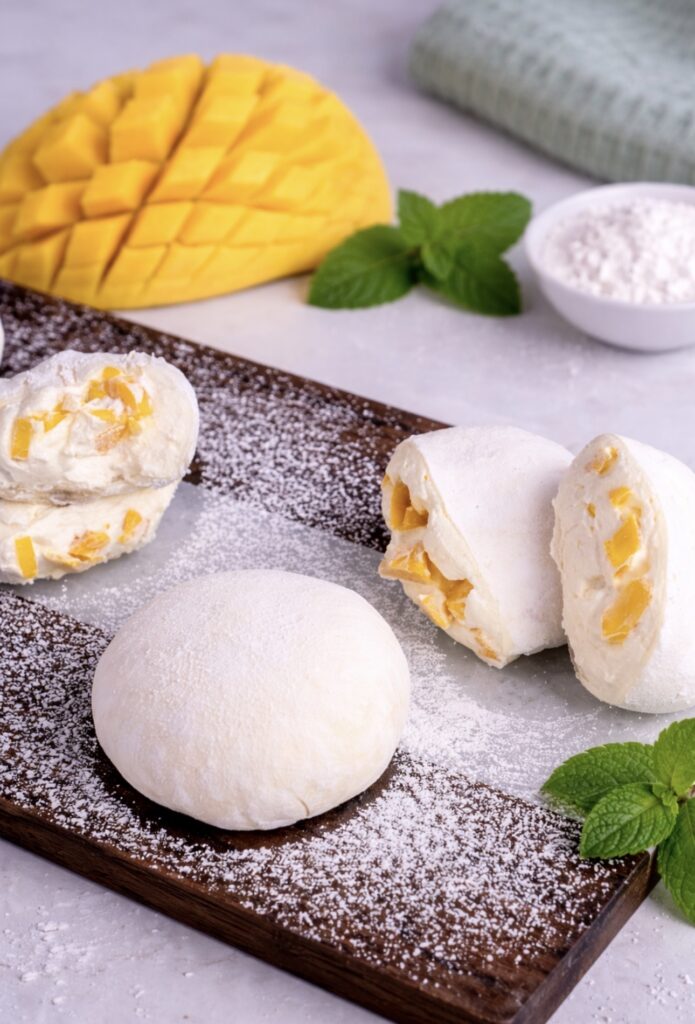 Mango mochi on a wooden board with one piece sliced to show filling