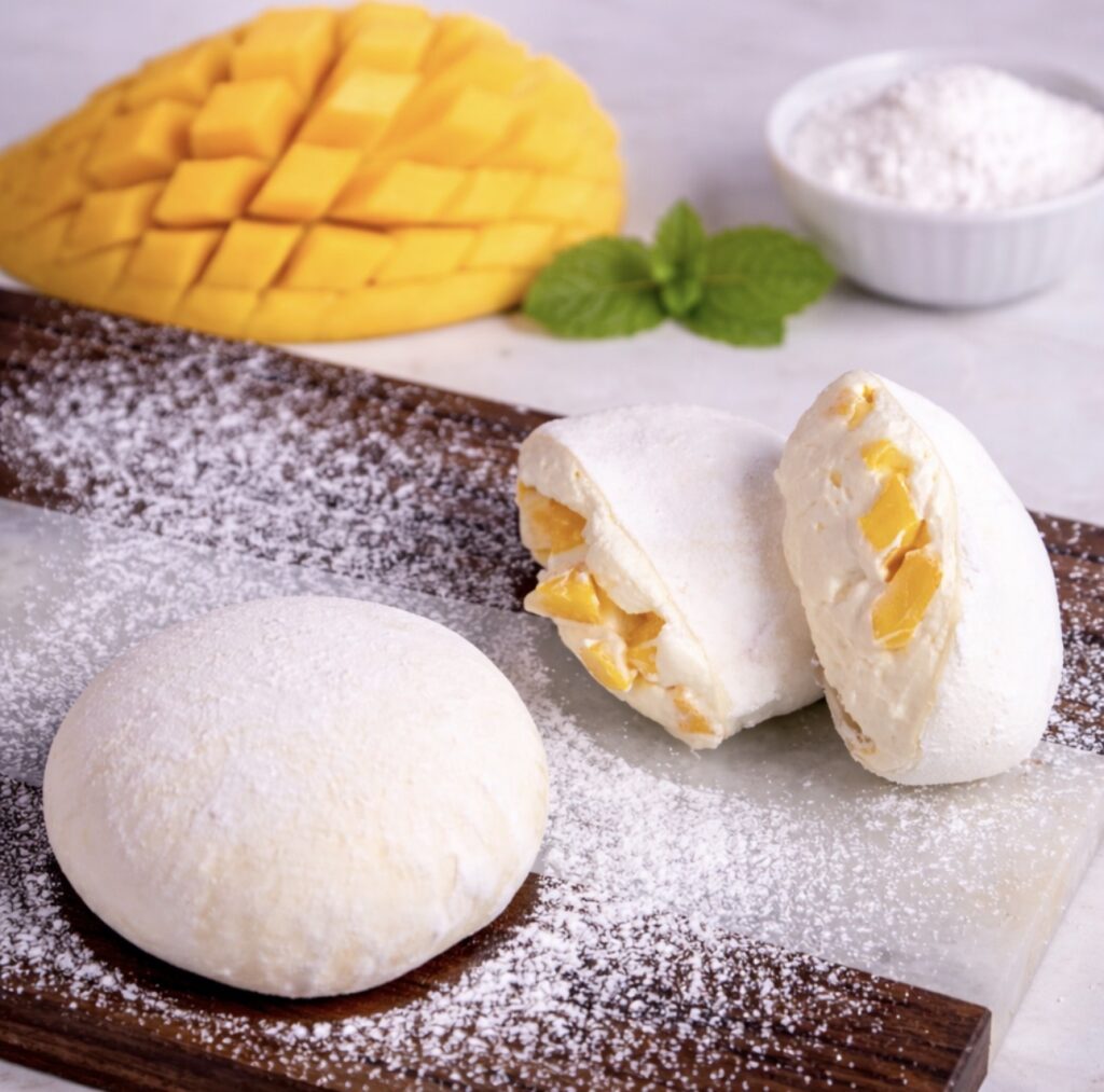 Mango mochi on a wooden board with one piece sliced to show filling