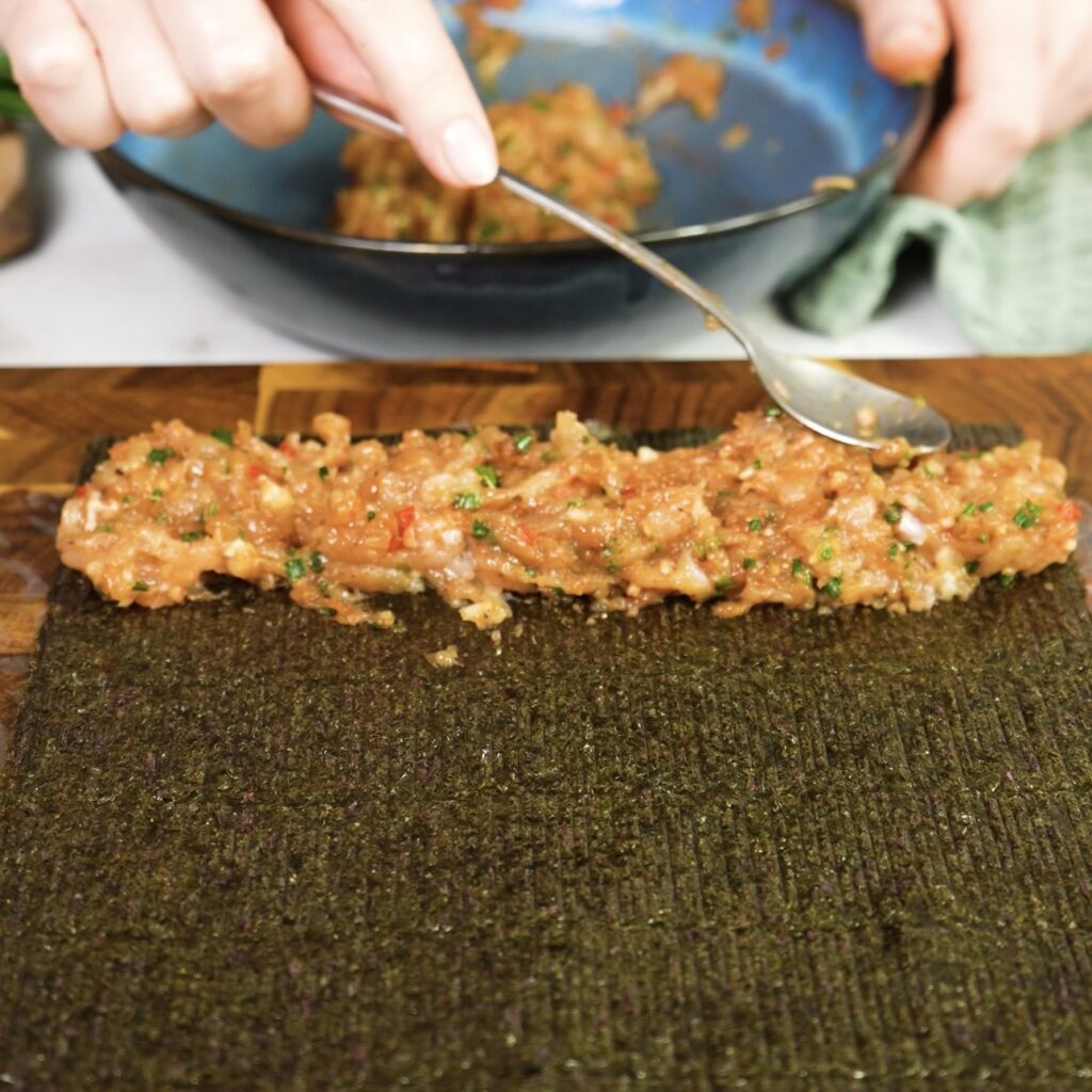 Nori sheet placed on rice paper with chicken filling added in a log shape