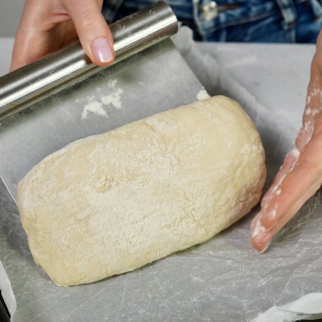 Transferring proofed ciabatta dough onto a lined baking tray