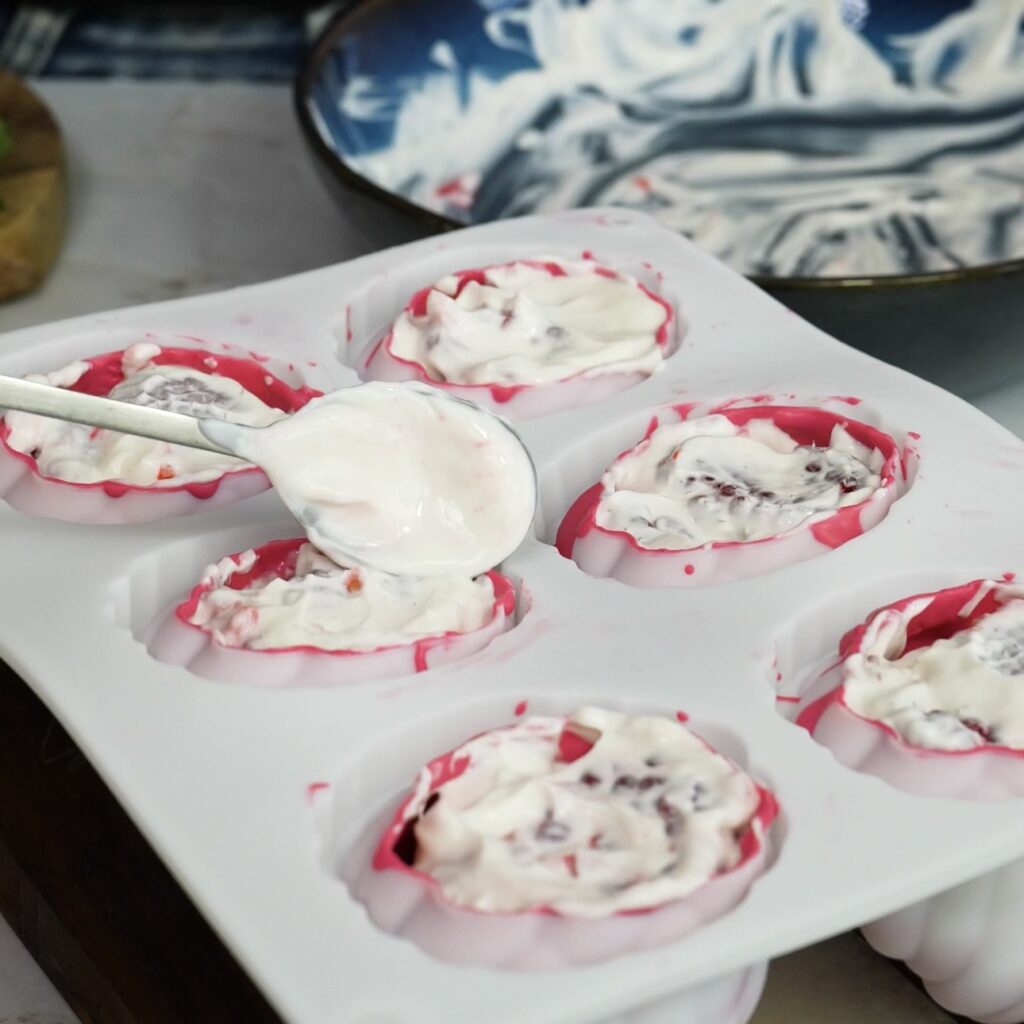 Adding raspberry yogurt filling to chocolate-coated mould cavities
